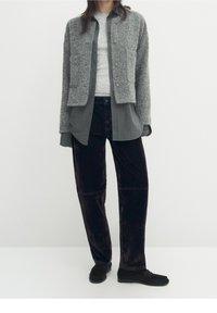 Szary strukturalny krótki żakiet, jasnoszara koszula, ciemne welurowe szerokie spodnie, czarne buty wsuwane. Minimalistyczny design z guzikami.
