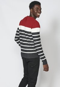 Maglione in maglia con un design a strisce rosso, bianco e navy. Collo rotondo, maniche lunghe, con colori a contrasto che creano un motivo audace.