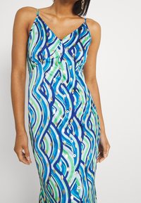 Robe maxi à motifs ondulés multicolores avec des accents bleus, verts et dorés ; dotée de bretelles ajustables et d'une fermeture à boutons sur le devant.