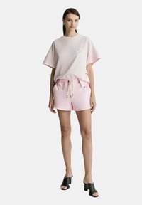 T-shirt oversize in cotone rosa con un piccolo cuore ricamato e pantaloni corti rosa abbinati. Sandali neri con tacco a strati completano l'outfit.