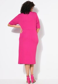 Fuksia midi-mekko lyhyillä hihoilla, teksturoidusta kankaasta ja istuvasta vyötäröstä, yhdistettynä matching vaaleanpunaisiin paksupohjaisiin sandaaleihin.