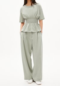 Světle zelený top s krátkým rukávem a nařaseným pasem; spárován s širokými kalhotami s vysokým pasem ve shodné barvě a bílou obuví.