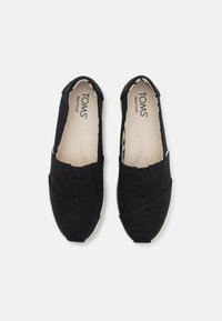 Schwarze Slipper aus Canvas mit runder Zehenpartie, Überkreuz-Design im Obermaterial und beige Sohle mit strukturiertem Finish.