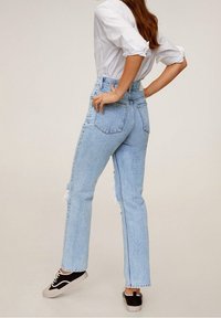 Jeans de tiro alto en azul claro con corte recto, presentan dobladillos deshilachados, un diseño clásico de cinco bolsillos y se combinan con zapatillas negras.
