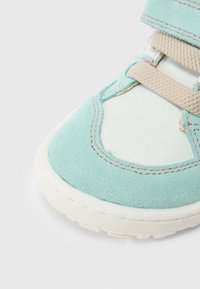 Πράσινο παπούτσι από σουέντ με λευκή δερμάτινη επιφάνεια, που διαθέτει μπεζ λουράκι και λεπτομέρειες ραφής. Χοντρή ελαστική σόλα με υφή.