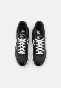Sneakers atletici in bianco e nero con materiale in pelle verniciata, caratterizzati da una punta arrotondata, lacci bianchi e accenti del logo a contrasto.