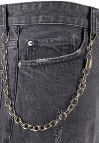 Melna denim bikses ar nolietojumiem, priekšējo kabatu un sudraba ķēdi, kas piestiprināta ar pievienotiem elementiem.
