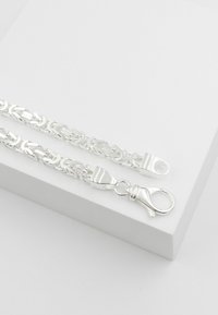 Silberne Kettenarmband mit miteinander verbundenen blattförmigen Gliedern, einem Karabinerverschluss und einer glatten, reflektierenden Oberfläche.