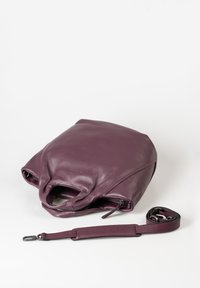 Borsa in pelle di un profondo viola con una texture morbida, dotata di chiusura con cerniera e tracolla rimovibile, adagiata su uno sfondo bianco.