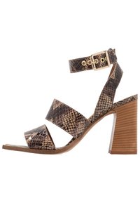 Blockhälssandal i strukturerad faux ormskinn i brunt och tan. Har flera remmar och en justerbar ankelsnäpp.