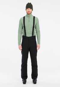 Zwarte sneeuwbroeken met verstelbare bretels, gecombineerd met een groen langemouwen top. De outfit heeft een aansluitend ontwerp en een gladde textuur.