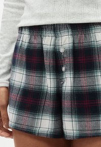 Βερμούδα καρό σε σκούρο μπλε, πράσινο και κόκκινο με ελαστική μέση και δύο κουμπιά μπροστά. Βαμβακερό ύφασμα με απαλή υφή.