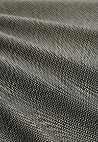 Textiel met een visgraatpatroon in zwart en crème, met een gestructureerd oppervlak en consistente golvende plooien door de stof.