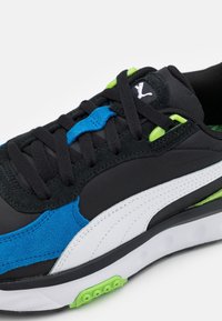 Baskets noires avec des accents bleus et verts, présentant une tige en suède texturé et mesh, une bande blanche et une semelle en caoutchouc à motif.