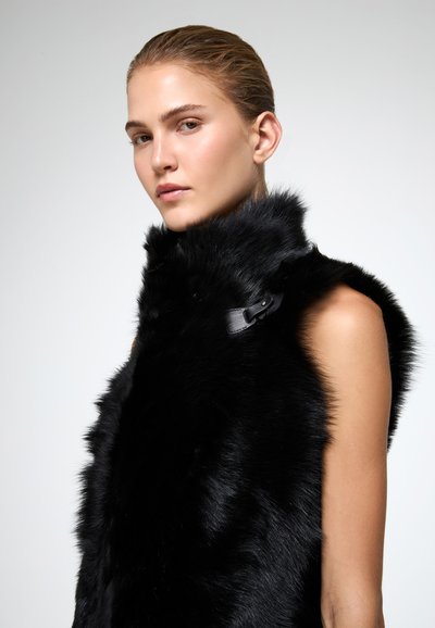 Juodas dirbtinis pūkinis liemenė su aukštu apykakle ir šoniniu odiniu užsegimu. turi minkštą, tekstūruotą paviršių ir be rankovių dizainą.