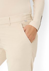 Beige corduroy broek met een ribbeltextuur en gestikte details, voorzien van zijzakken en een label nabij de tailleband.