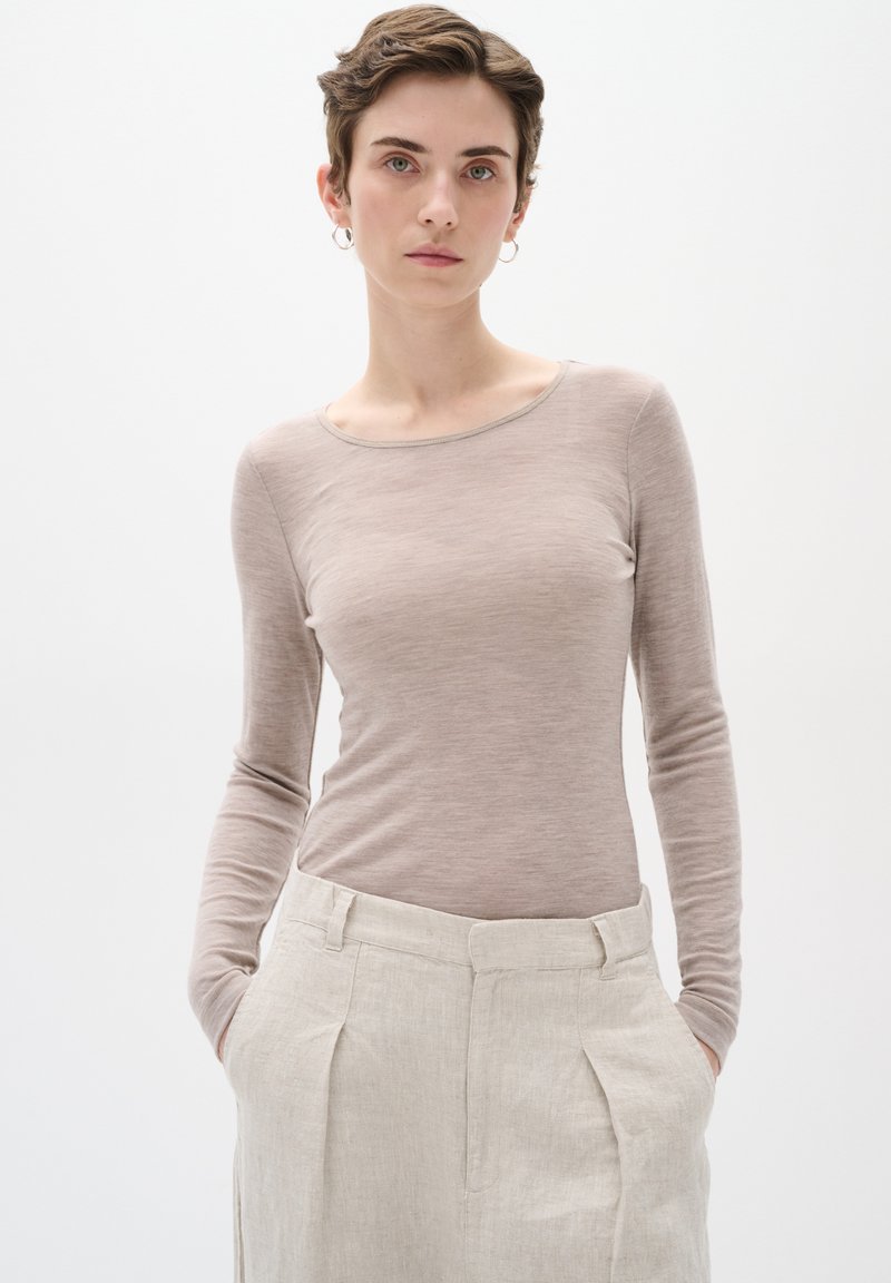 Top a maniche lunghe di un leggero color taupe, realizzato in un tessuto morbido e leggero, con scollatura a barca, abbinato a pantaloni beige in lino a vita alta.