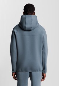 Lichtblauwe hoodie met een grote capuchon, naadloos schouderontwerp en ribgebreide manchetten. Gladde textuur en minimalistische stikdetails.