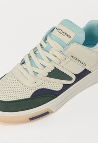 Sneaker with perforated cream leather and green, dark blue, and light blue accents. Features a textured design and cream laces.