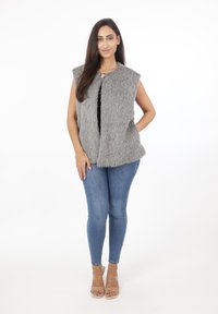 Szary kamizelka z futra sztucznego z otwartym przodem, bez rękawów, teksturowana powierzchnia. Połączona z niebieskimi dżinsami skinny i sandałami na obcasie z przezroczystymi paskami.