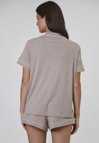 Beige Baumwoll-Pyjama-Set mit einem kurzärmligen Oberteil mit Kragen und weißem Saum, kombiniert mit passenden Shorts mit umgeschlagenen Säumen und Saum.