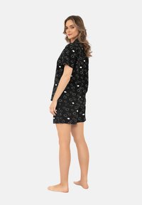 Czarny komplet piżamowy z krótkim rękawem, składający się z luźnej bluzki i szortów, ozdobiony białym wzorem w zwierzęta na miękkim materiale.