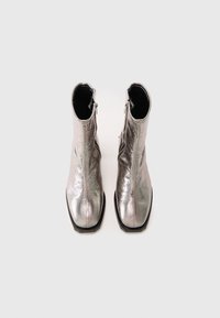 Botas de tobillo metálicas plateadas con un acabado texturizado, cremalleras laterales y punta cuadrada, con una suela negra y forro interior.