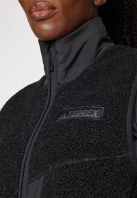 Black fleece vest with a high collar, featuring a textured exterior, smooth fabric accents, and a prominent black Terrex logo.