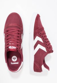 Para bordowych sneakersów Hummel z białymi paskami w kształcie chevron i białymi podeszwami, jeden pokazujący widok z góry, a drugi z boku.