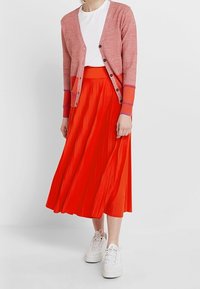 Falda midi plisada roja combinada con un cárdigan rosa y una camiseta blanca. El look se completa con zapatillas blancas.