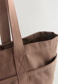 Brązowa torba na ramię z materiału, charakteryzująca się teksturowaną powierzchnią, solidnymi uchwytami i kieszonką zewnętrzną, zaprojektowana z wzmocnionymi szwami.