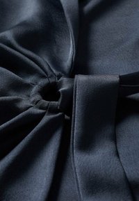 Tummansininen kangas, jossa on sileä textura, solmittu yksityiskohta ja pehmeät laskokset, jotka korostavat sen laskeutumisominaisuuksia.
