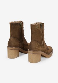 Stivali alla caviglia in suede marrone con tacco quadrato, dotati di cerniera laterale, occhielli in metallo per i lacci e suola testurizzata.
