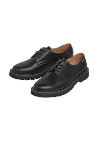 Scarpe nere in pelle con finitura liscia, punta tonda, dettaglio di allacciatura, suola in gomma e cucitura bianca lungo il bordo della suola.