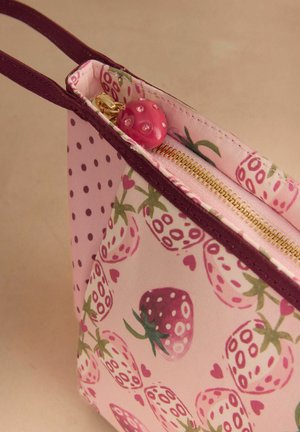 Pieni vaaleanpunainen kangaspussi, jossa viininpunainen reuna, mansikkakuosi, kultainen vetoketju ja vaaleanpunainen helmillä koristeltu vetoketjun vedin.