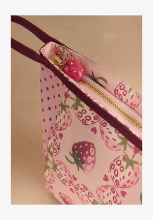 Pieni vaaleanpunainen kangaspussi, jossa viininpunainen reuna, mansikkakuosi, kultainen vetoketju ja vaaleanpunainen helmillä koristeltu vetoketjun vedin.