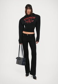 Felpa nera cropped con logo rosso, jeans neri a zampa d'elefante, stivali neri con tacco alto e una borsa strutturata blu navy con dettaglio della fibbia.