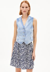 Jeansweste in Hellblau mit V-Ausschnitt und fünf silbernen Knöpfen, kombiniert mit einem floral gemusterten Rock in Marineblau und Weiß.