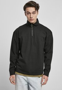 Zwarte sweatshirt met ritssluiting heeft een hoge kraag, lange mouwen en een losse pasvorm. Gemaakt van een soepele katoenmix met minimale stikdetails.