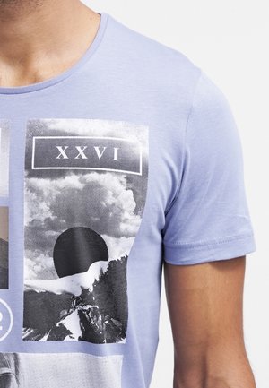 Lyse lilla t-shirt med sort-hvid grafik af bjerge, skyer, en mørk sol og romerske tal XXVI på brystet.