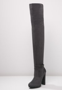 Botas gris de ante hasta la rodilla, con un alto tacón cuadrado y un detalle de hebilla en el tobillo para añadir un toque adicional.