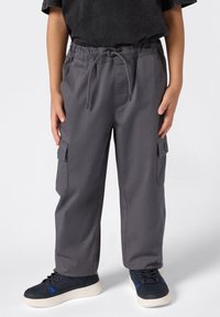 Szare spodnie cargo z elastycznym paskiem i sznurkiem. Posiadają boczne kieszenie i luźny krój, zestawione z ciemnymi trampkami.