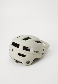 Cască de culoare bej deschis, cu deschideri de ventilație, rotiță de ajustare a dimensiunii și branding. Prezintă un design aerodinamic pentru confort și siguranță.