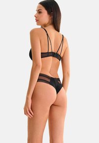 Ensemble de lingerie noire comprenant un soutien-gorge en maille transparente avec des bretelles ajustables et un string assorti avec des accents en dentelle. Texture lisse, couverture minimale.