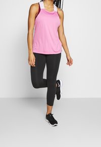 Top de entrenamiento rosa con diseño de espalda nadadora, combinado con leggings negros y zapatillas negras. Textura suave, forma ajustada y tejido transpirable.