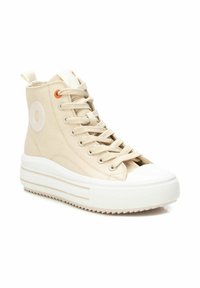 Zapatillas altas de lienzo beige con puntera de goma blanca y suela de plataforma en capas. Presentan ojales naranjas y un parche con el logo en el costado.