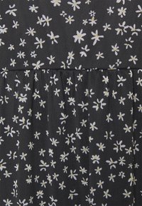 Svart tyg med små vita och gula blommönster samt samlade sömmar.