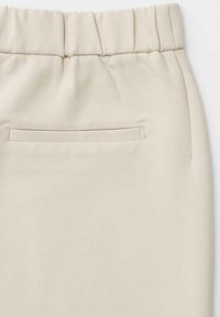 Beiger Rock mit einem gerafften, elastischen Bund und einer diskreten Rückentasche mit horizontaler Öffnung. Glatte Textur, leichter Stoff.