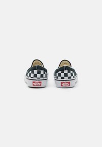 Paire de chaussures Vans slip-on à motif damier noir et blanc vue de dos avec logos rouges "Off The Wall" sur les semelles blanches.