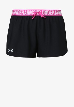 Mujer vistiendo un sujetador deportivo negro y shorts negros de Under Armour con cintura rosa y zapatos deportivos negros, de pie sobre fondo gris.